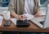 Przedsiębiorca liczy koszty na kalkulatorze przy laptopie na biurku