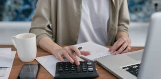 Polisa od utraty dochodu dla przedsiębiorcy jednoosobowego a realna ochrona finansowa Przedsiębiorca liczy koszty na kalkulatorze przy laptopie na biurku