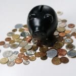 Czarna skarbonka otoczona monetami jako symbol oszczędności i finansów