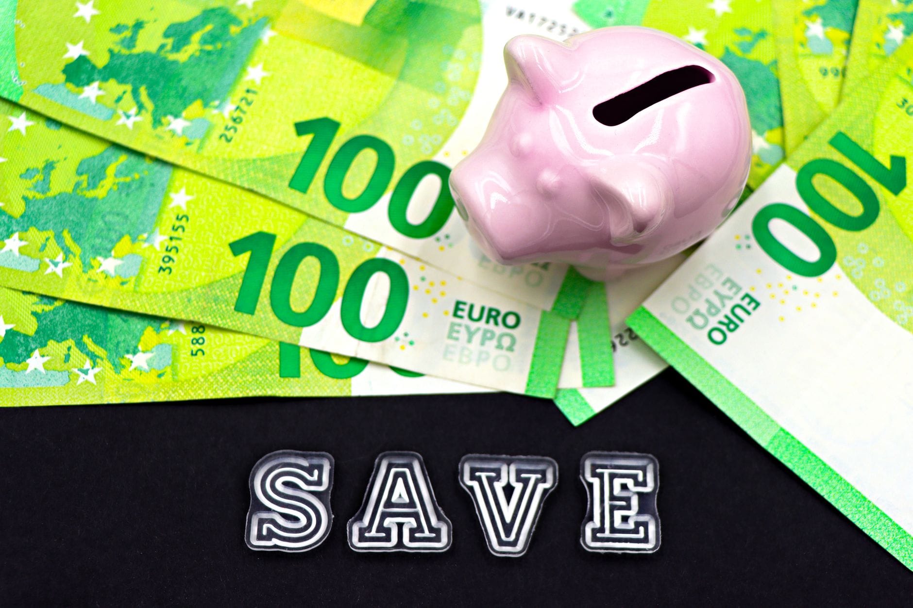 Różowa skarbonka na banknotach euro z napisem save symbolizująca oszczędzanie